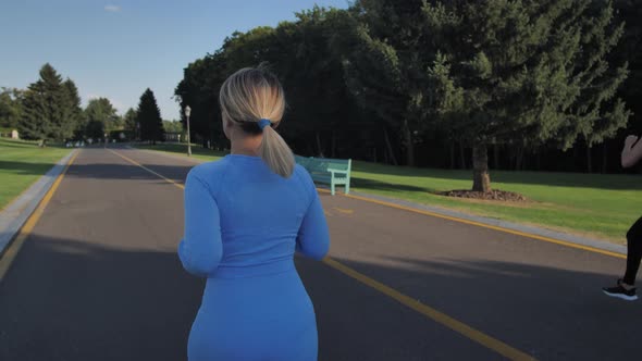 Sporty Young Woman Jogging Along Walkway in Park alt