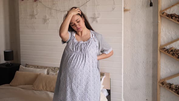 Portrait of a Pregnant Woman in Home Pajamas and a Bathrobe with Back Pain alt