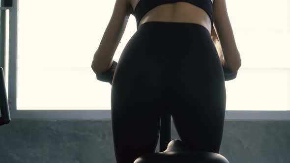 Rear View of Sporty Woman Riding Stationary Bike at the Gym alt