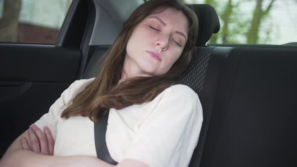 Young Woman Sleeps in the Back Seat of a Car