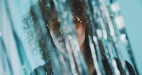 Seductive curly girl with sunglasses dancing through a glitter curtain alt