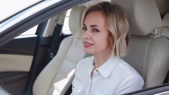 Smiling Business Woman in White Shirt Sitting in the Car and Drinking Coffee alt