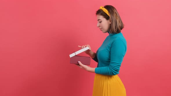 Close Up of a Happy Woman Opening Gift Box Over Red Background. alt