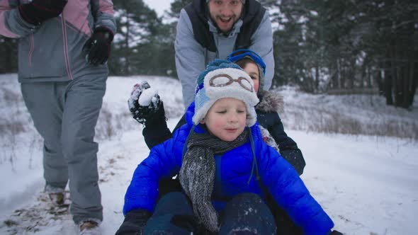 Joyful Childhood Happy Male Children Have Fun Sledding Together with Their Parents in Snowy Forest