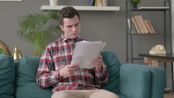 Man Reacting to Loss on Documents Sofa alt