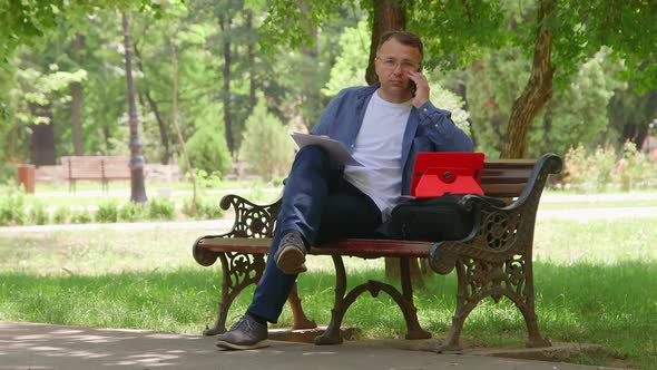 Man Sitting on the Bench and Working Outdoors.