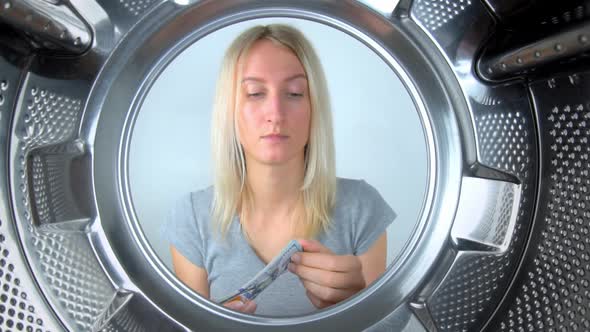 housewife counts money near washing machine and leaves them to wash. alt