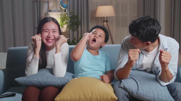 Asian Family Celebrating While Watching Tv Together Sitting On A Sofa In The Living Room At Home alt