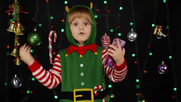 Kid Girl Christmas Elf Santa Helper Types Something on Mobile Phone Enjoys Browsing Social Media alt
