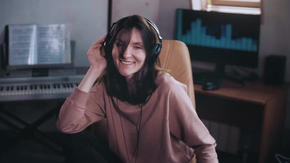 A beautiful girl with headphones listens to music in a chair at the computer. Dancing and smiling.