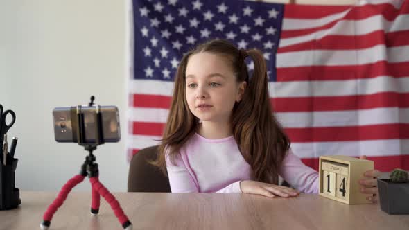 A Schoolgirl Tells a Video About American Flag Day on the Camera of a Smartphone Standing on a Table alt