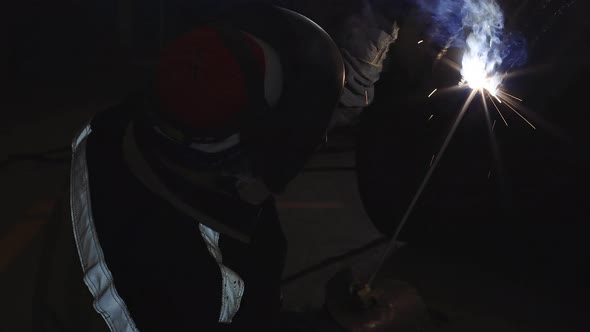 A Welder in Protective Clothing Works in a Dark Workshop