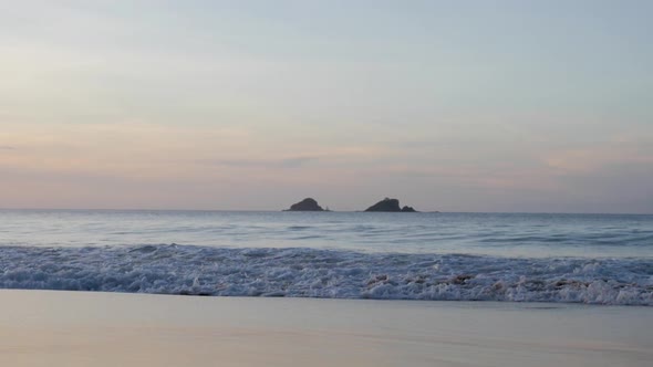Ultra slow motion shot of waves breaking and swashing at beach with beautiful colourful sky at dusk alt
