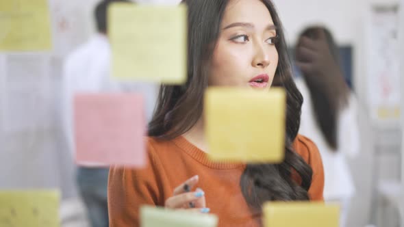 Asian business creative team meeting by use post it notes to share idea on glass wall. alt