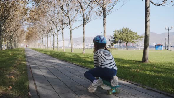 A Girl Sitting on a Skateboard and Pushing Herself with a Leg Steadicam