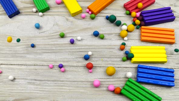Multi-colored plasticine balls roll on a wooden board with plasticine lying on it, slow motion alt