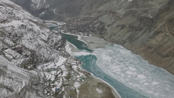 Aerial Flying Over Frozen Valley With Turquoise River Running Through With Tilt Up View Of Snow Capp alt