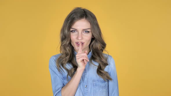 Young Girl Gesturing Silence, Finger on Lips, Yellow Background alt
