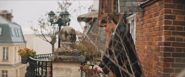 Young man standing on a balcony looking down the street alt