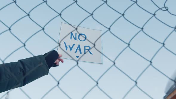 Closeup Sign with Inscription No War in the Blue Sky Through the Fence Bars alt