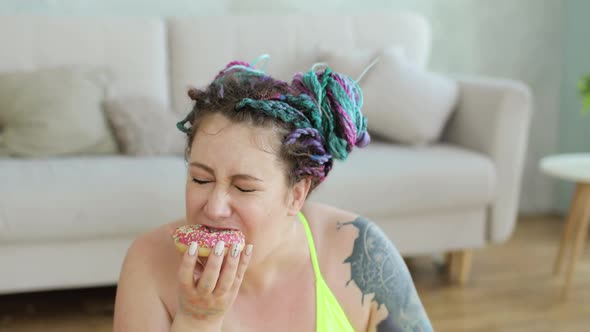 Woman in Sportswear Enjoying of Eating Donut Sitting on Fitness Mat at Home