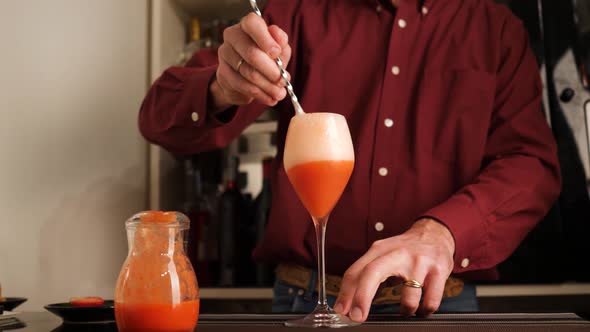 Barman prepares an Italian cocktail called Fragolino with strawberry juice and sparkling wine.