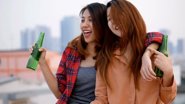Slow-motion young Asian woman lesbian couple clinking bottles of beer party on the rooftop. alt