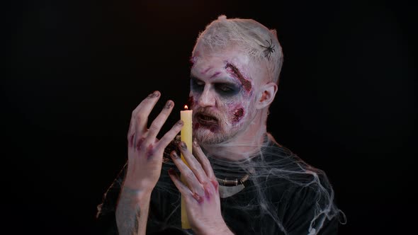 Zombie Man with Makeup with Fake Wounds Scars and White Contact Lenses Spells Conjures Over a Candle alt