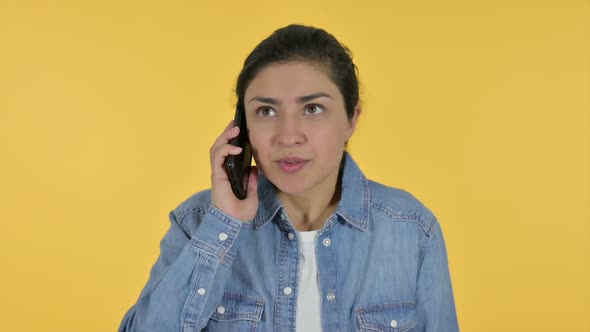 Angry Indian Woman Talking on Smartphone Yellow Background alt