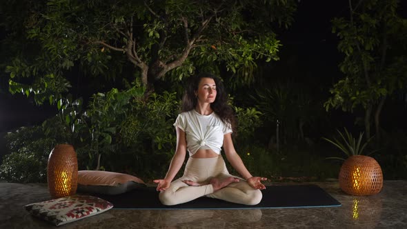 Woman Enjoys Yoga in Lotus Position on Black Mat at Night