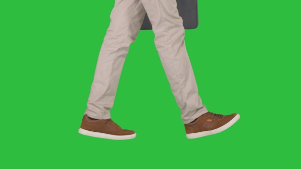 Mans feet is walking in jeans and sneakers on a Green Screen alt