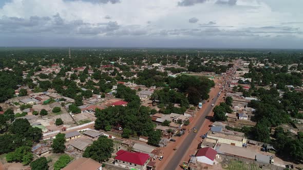 Lowering aerial view of Brikama in The Gambia showing lush green trees and main street alt