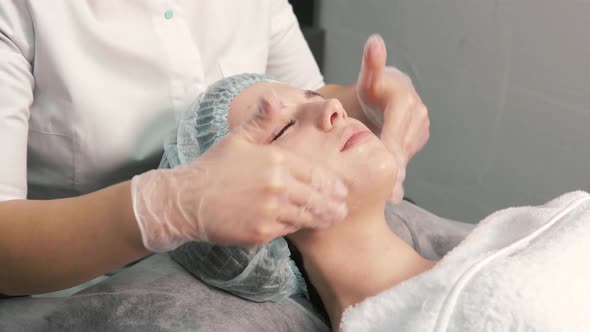 The Hands of the Cosmetologist in Gloves Do a Facial Massage of the Client