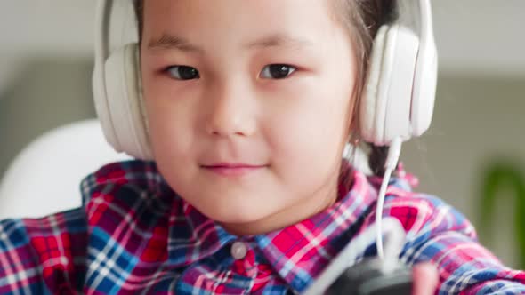 Little Asian Girl in Headphones Listening to Music on Smartphone and Dancing