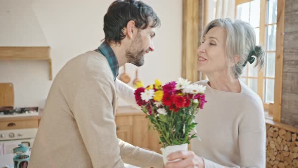 Happy Adult Son Greeting His Senior Mother with Bouquet of Flowers Grateful Grey Haired Lady alt