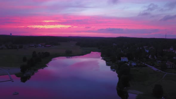 Aerial descending, drone view backwards, above a lake and a town, purple sky, at a colorful sunset o alt