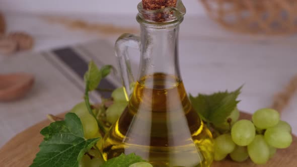 Rotating Jug or Bottle with Grape Oil Against Green Grapes on a Wooden Background