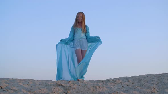 Angelic Girl in Waving Blue Tunic in Sandy Desert on Clear Sky Landscape. Happy Teen Girl in Blue alt