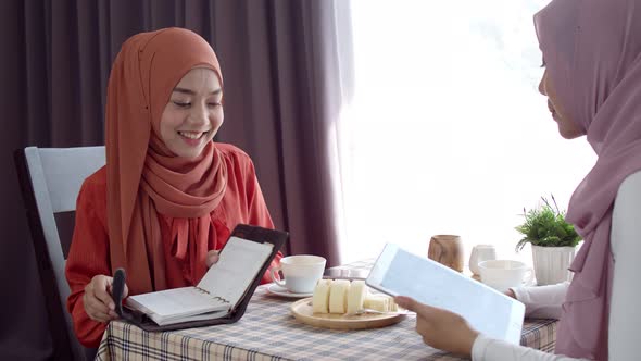 Two young muslim woman discussing and working in coffee shop