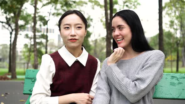 Two Female Women Friends Gossiping and Pointing at Someone Out in Public Park alt
