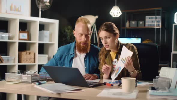 Young Business Couple Showing Documents in Front of Laptop Screen in Office alt