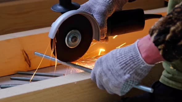 A builder's hands in work gloves cut a metal hairpin with an angle grinder electric tool. Preparatio alt