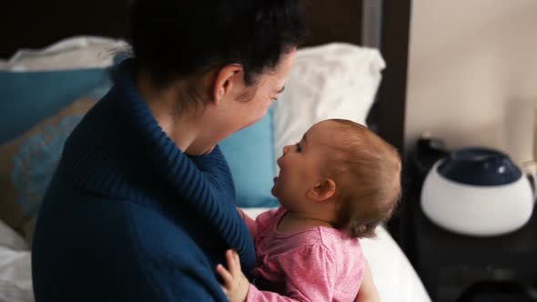 Mother embracing baby girl in living room alt