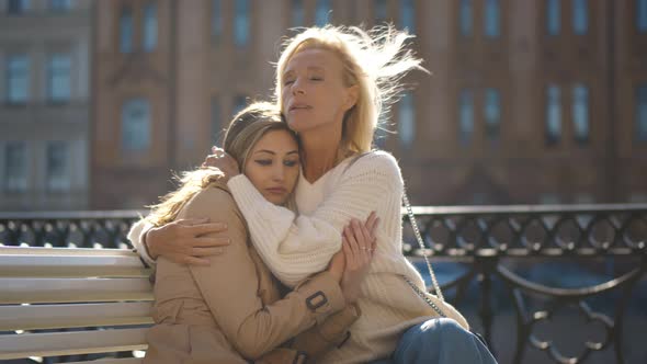 Daughter with Senior Mother Sitting on City Bench and Hugging alt