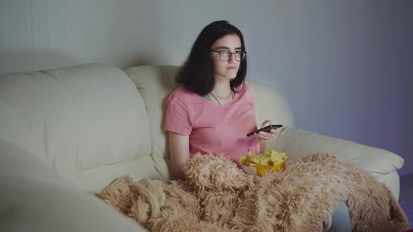 Girl Relaxing Near Tv in the Evening Uses the Phone with Potato Chips