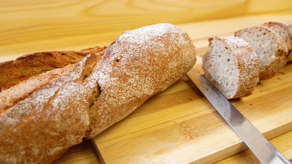 Fresh Crispy Baguette Lies on a Cutting Wooden Board Next to Cut Pieces and a Knife
