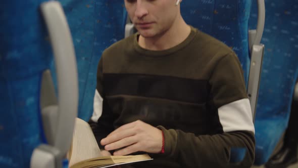 A Young Man is Reading a Book on the Train Looking Out the Window