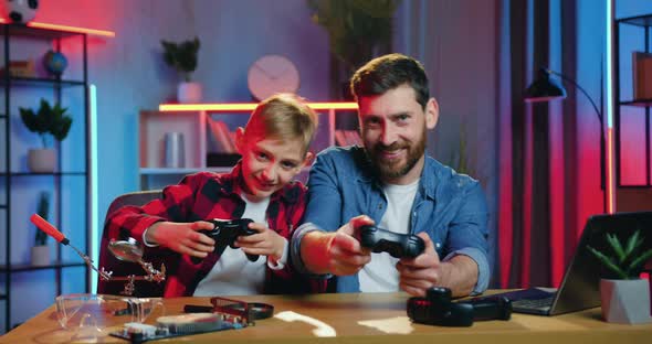Bearded Dad and Teen Son Enjoying Videogames and Celebrating Victory alt
