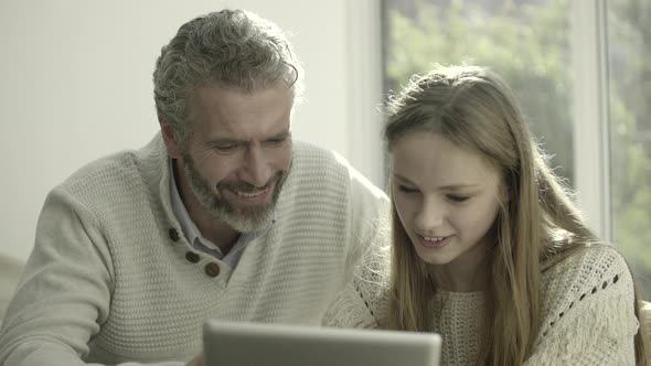 Father and teenage child at home looking at digital tablet