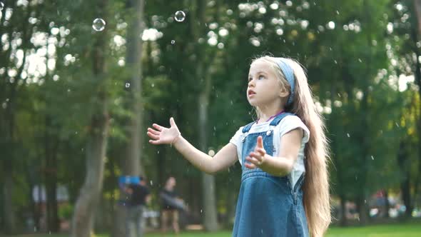 Little happy child girl chasing soap bubbles outdoors in summer park alt